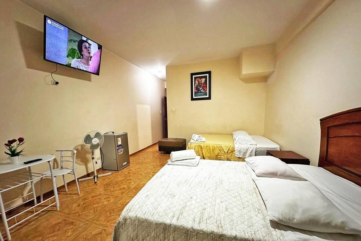 A hotel room with a bed, bedside table, chair, desk, and a television mounted on the wall.