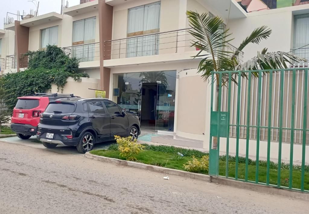 Un edificio moderno con entrada porticada, un coche estacionado frente a él y un pequeño jardín.