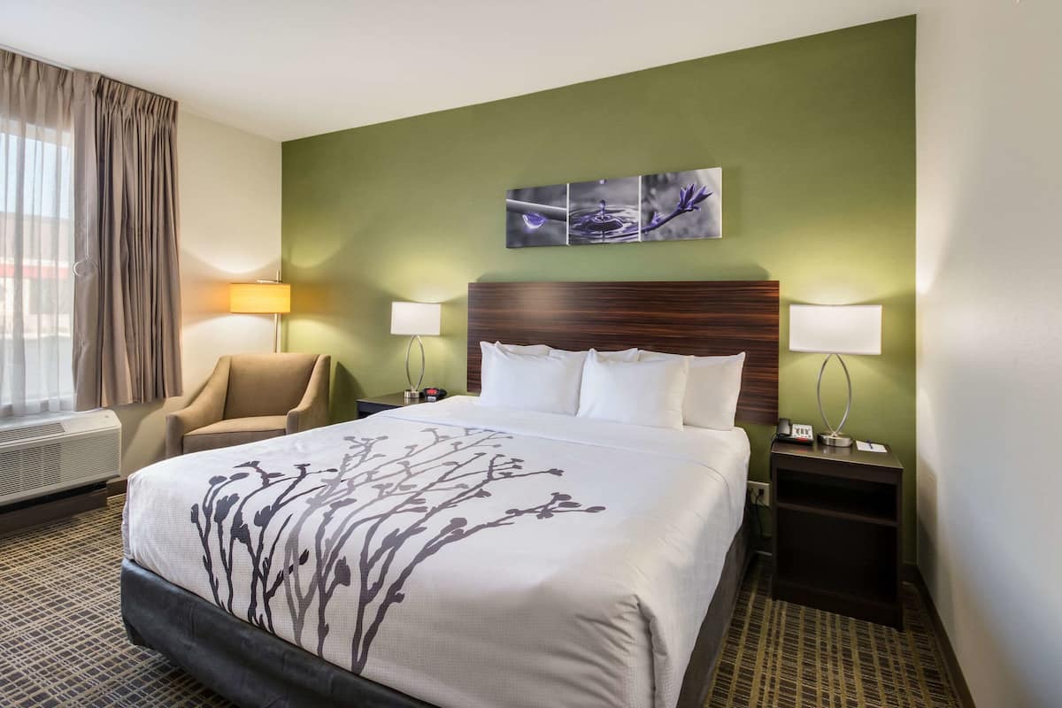 Een hotelkamer met een groot bed, twee nachtkastjes met lampen, een stoel en een raam met gordijnen.