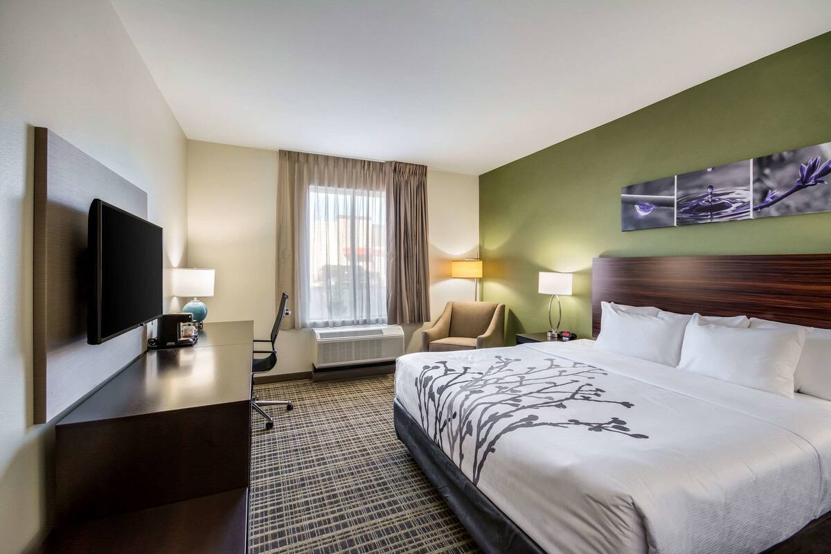 Een hotelkamer met een groot bed, een flatscreen televisie, een bureau met lamp, een stoel en een raam met gordijnen.
