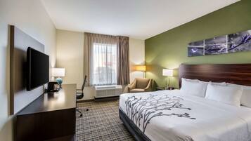 Ett hotellrum med en stor säng, en platt-TV, ett skrivbord med en lampa, en stol och ett fönster med gardiner.