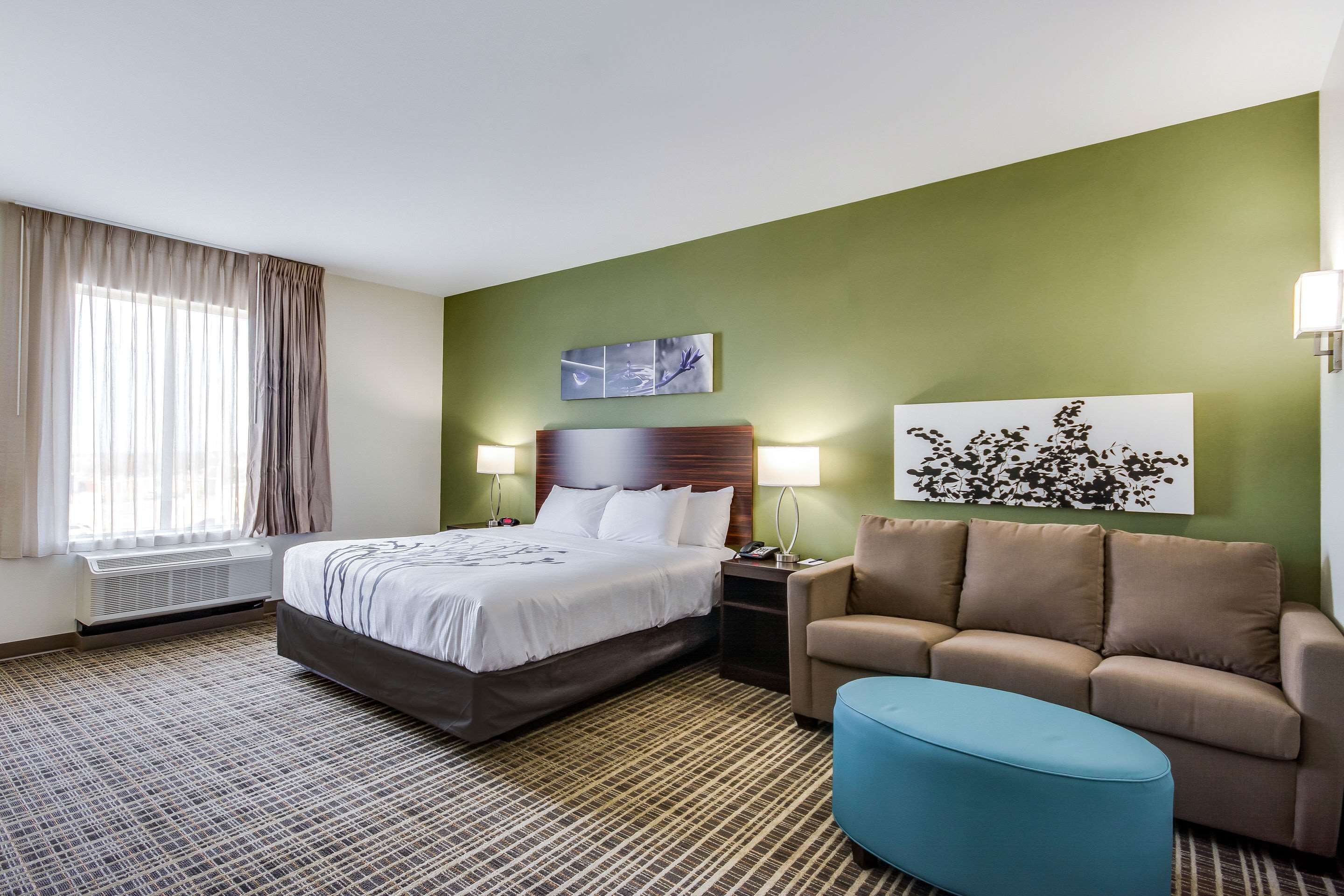 Ein Hotelzimmer mit Bett, einer Sitzecke, einem Couchtisch, einer Wand mit Kunstwerken und einem Fenster mit Vorhängen.