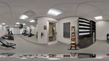 A gym with exercise equipment, a wall-mounted medicine ball rack, and a mirror reflecting the room.