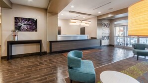 A modern reception area with a dark wood floor, a reception desk, a blue armchair, and a large window with a view. - Sleep Inn & Suites Yukon Oklahoma City (Yukon)