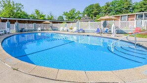 Una piscina circular con valla blanca, sillas de descanso y una zona cubierta con sombrilla.