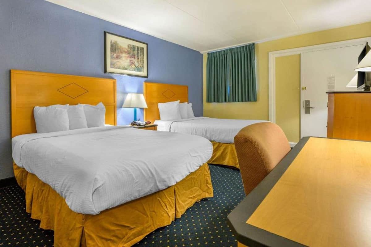 A hotel room with two beds, a desk, and a chair.