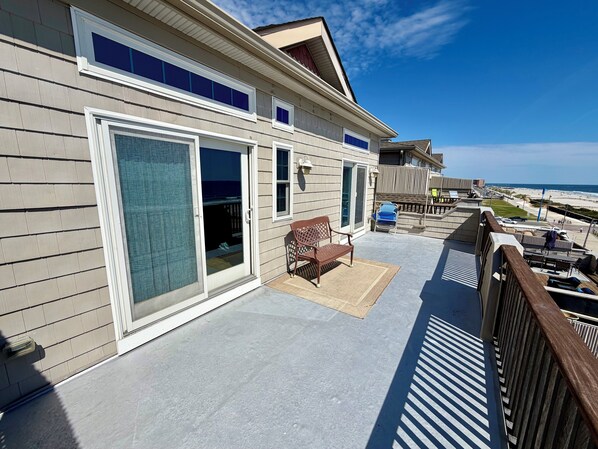 A beachfront property with a covered patio, a sliding glass door, and a view of the ocean. - Panoramic Ocean Views, 2 Large Decks, and Direct Beach Access! (North Wildwood)