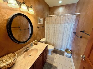 A bathroom with a large mirror, a sink, a toilet, and a shower curtain.