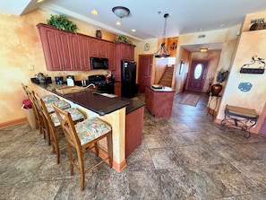 A kitchen with a central island, bar stools, wooden cabinets, and a staircase leading to another level. - Panoramic Ocean Views, 2 Large Decks, and Direct Beach Access! (North Wildwood)