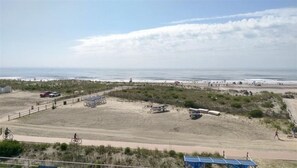 A beach area with a dirt path, parked vehicles, and a few people.