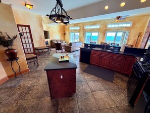 A spacious kitchen with a central island, a dining area with a sofa and chairs, and a view of the outdoors through large windows. - Panoramic Ocean Views, 2 Large Decks, and Direct Beach Access! (North Wildwood)