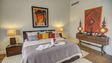 A neatly arranged bedroom with a bed, two bedside tables, a dresser, and a wall with a painting and a tapestry.