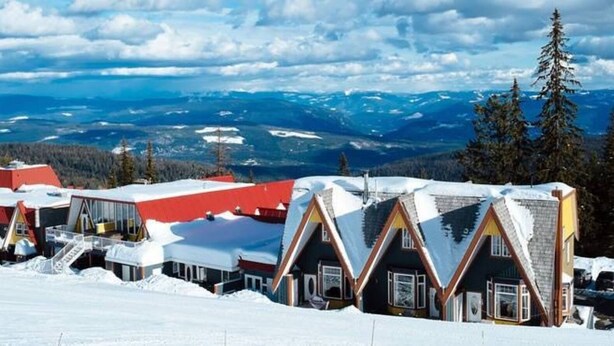 Een rij chalets met puntige daken, gelegen in een besneeuwd landschap met bergen in de verte.