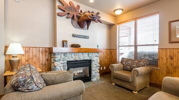 A cozy living room with a stone fireplace, wooden paneling, and a mounted deer head.