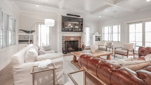 A spacious living room with a fireplace, leather sofa, and a high ceiling with exposed beams. - 5 star, grand 8 BR estate, large yard, pool, pond, walk to town & beach (Nantucket)
