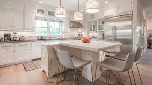 A modern kitchen with white cabinetry, a central island, and stainless steel appliances. - 5 star, grand 8 BR estate, large yard, pool, pond, walk to town & beach (Nantucket)