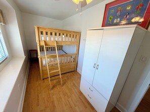 A room with a bunk bed, a white wardrobe, and a window with blinds.