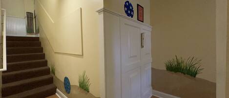 Una escalera con un rellano alfombrado, una puerta blanca con un pequeño ventanal y una pared con un cuadro enmarcado y un plato decorativo.