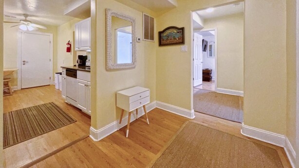 A hallway with a kitchen area, a white console table, a mirror, and a framed picture on the wall.
