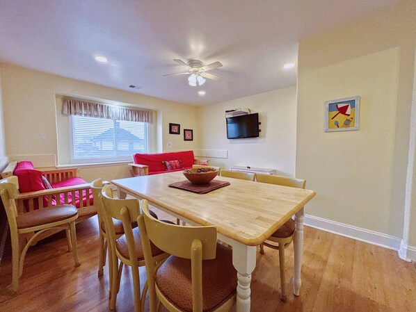 A dining area with a wooden table, four chairs, a red sofa, and a television on the wall.
