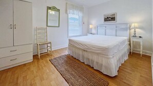 A bedroom with a bed, a wardrobe, a chair, a bedside table, a lamp, a ceiling fan, and a window with blinds.