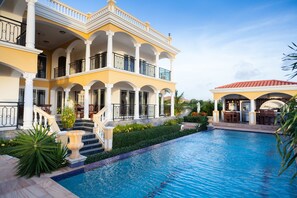 Une grande maison à deux étages, avec une piscine en premier plan.