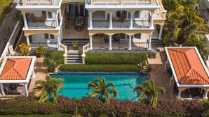 Une grande maison à deux étages, dotée d’une piscine, de plusieurs balcons et d’un jardin bien entretenu.