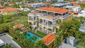 Un immeuble résidentiel à plusieurs étages, doté d’une piscine, entouré d’une végétation luxuriante et d’autres maisons.