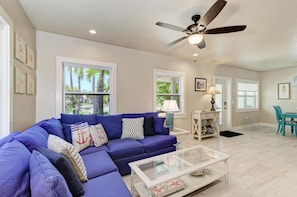 Relax in this inviting living room with a large sofa, dining area, and ceiling fan.