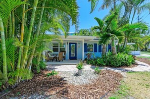 Une maison avec une porte bleue, une terrasse avec des chaises et une végétation tropicale luxuriante.
