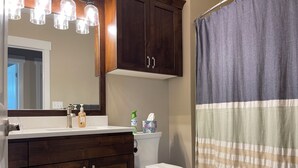 Un baño con tocador de madera, inodoro blanco, espejo y cortina de ducha a rayas.