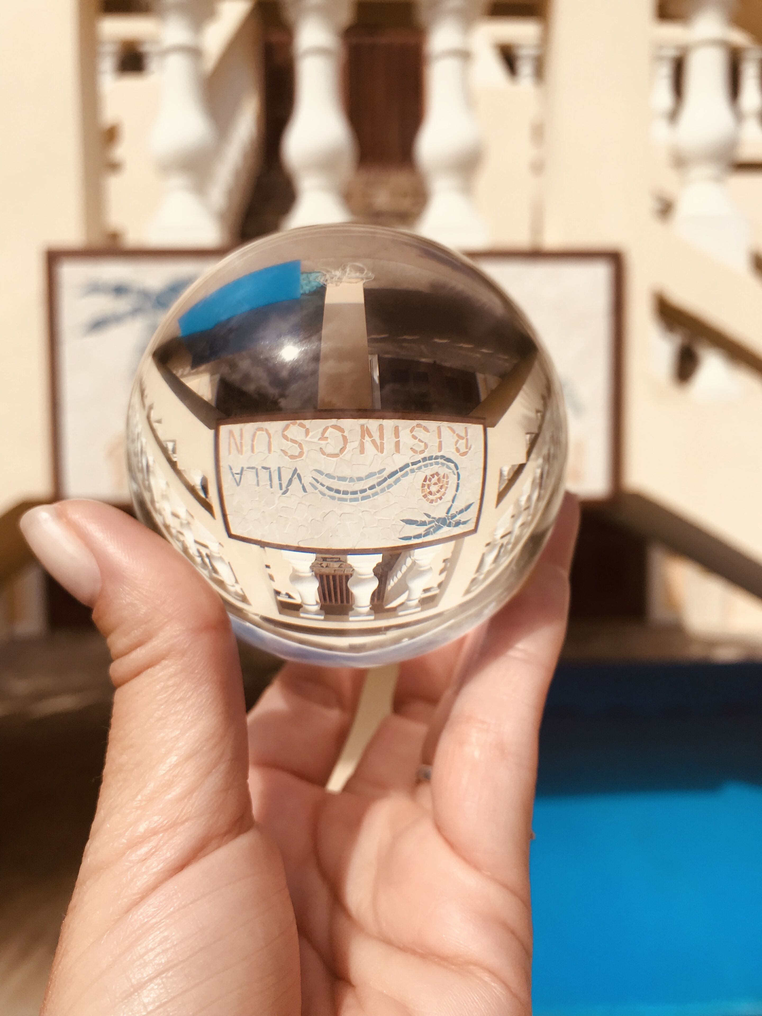 A hand holding a clear, round object with the text "RINOSUS VILLA" and decorative elements.