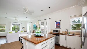 A modern kitchen with white cabinetry, a wooden island, and a dining area with a white sofa.
