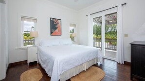 A bedroom with a large bed, two bedside tables, a ceiling fan, and a view of a balcony with plants.