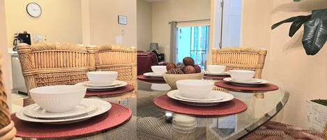 Un coin repas avec une table à plateau en verre, des chaises en osier, des assiettes et des bols blancs.