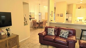 A living room with a brown leather sofa, a television, and a dining area with a table and chairs. - Platinum rated 2BR ground floor next to pool big screen TVs, Huge patio, wifi (Davenport)