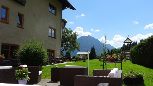 A building with outdoor seating, a grassy area, and mountains in the background. - Beautiful Family Apartment (Hinterbichl)