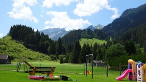 A playground with slides and swings, surrounded by a grassy field and a mountain backdrop. - Beautiful Family Apartment (Hinterbichl)