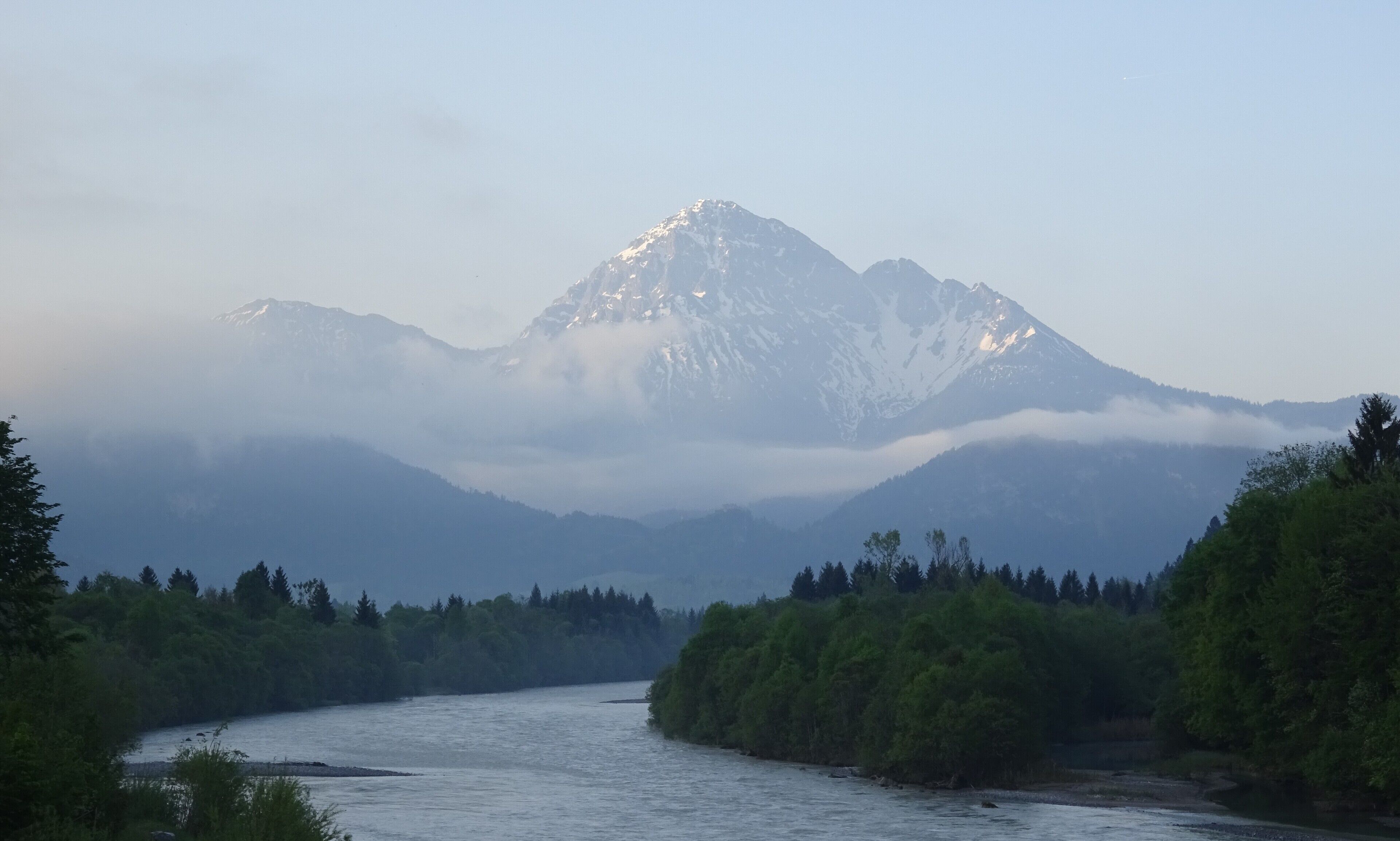 Un río serpentea por un bosque con una montaña al fondo.