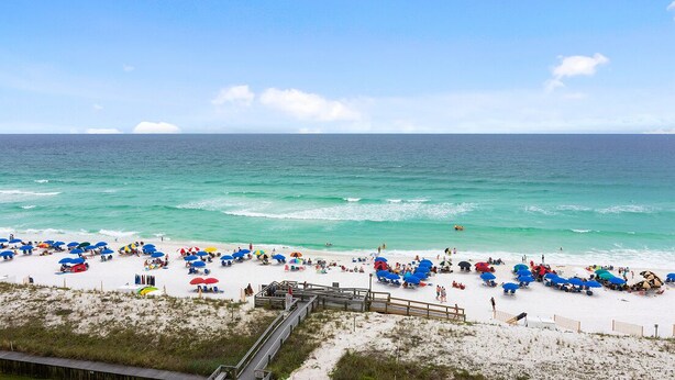 A beach with white sand, a wooden boardwalk, and a clear blue sky.