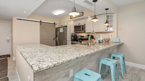 A kitchen with a granite countertop, stainless steel appliances, and teal bar stools.