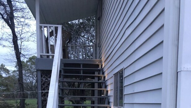 A staircase leading to a house with white siding and a covered porch area. - The Farmhouse (Baton Rouge)
