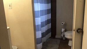 Un baño con una cortina de ducha a rayas, un inodoro y dos alfombras en el suelo.