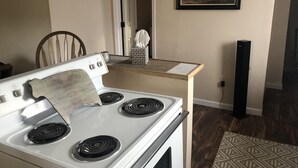 A kitchen with a white stove, a wooden chair, a small table with a tissue box, and a framed picture on the wall. - The Farmhouse (Baton Rouge)