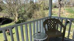 A wooden deck with a white railing, a glass table, and two plastic chairs. - The Farmhouse (Baton Rouge)