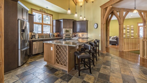 A spacious kitchen with a large island, dark wooden cabinets, and a stone tile floor.