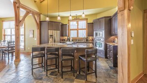 A spacious kitchen with a large island, dark wooden cabinets, and a stone tile floor.