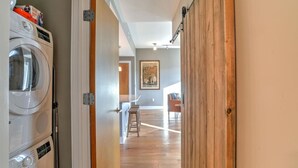 Un lavadero con lavadoras apiladas y una puerta de madera que da a un pasillo con comedor.