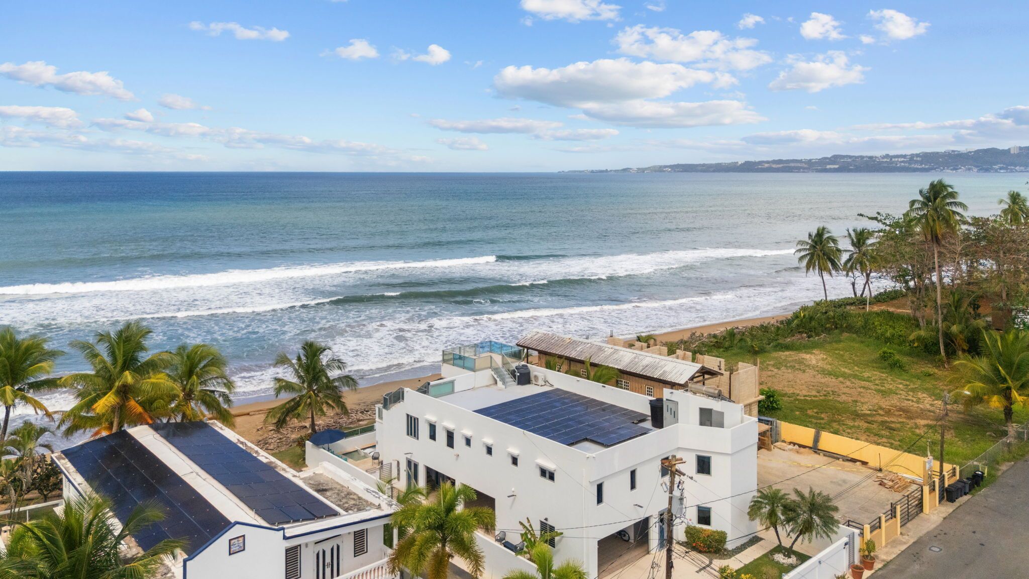 Vista costera con playa, océano y edificios residenciales con paneles solares.