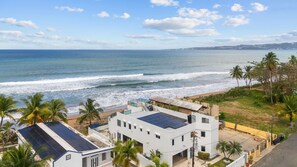 A coastal view with a beach, ocean, and residential buildings with solar panels.